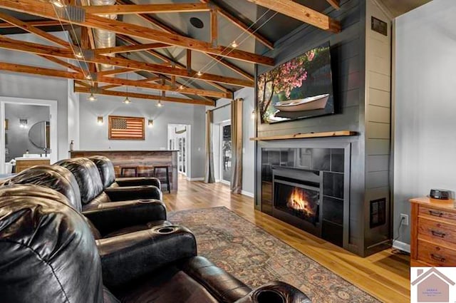 living room featuring light hardwood / wood-style floors, high vaulted ceiling, beamed ceiling, and a tile fireplace