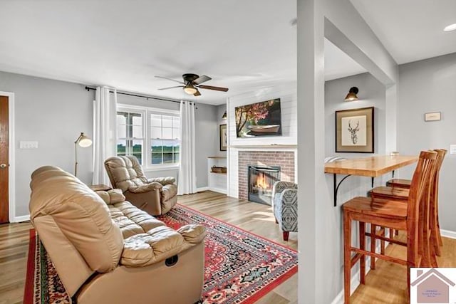 living room with a fireplace, light wood-type flooring, and ceiling fan