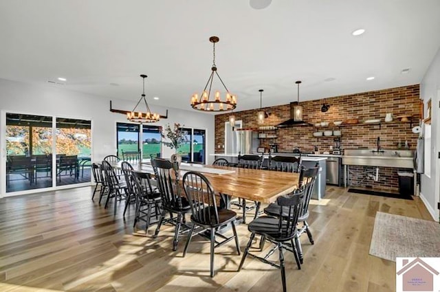 dining area with light hardwood / wood-style flooring, an inviting chandelier, and brick wall