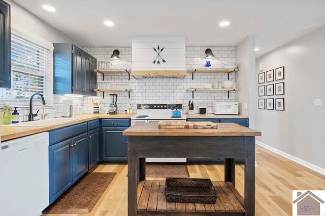 kitchen with backsplash, blue cabinetry, light hardwood / wood-style floors, sink, and white appliances