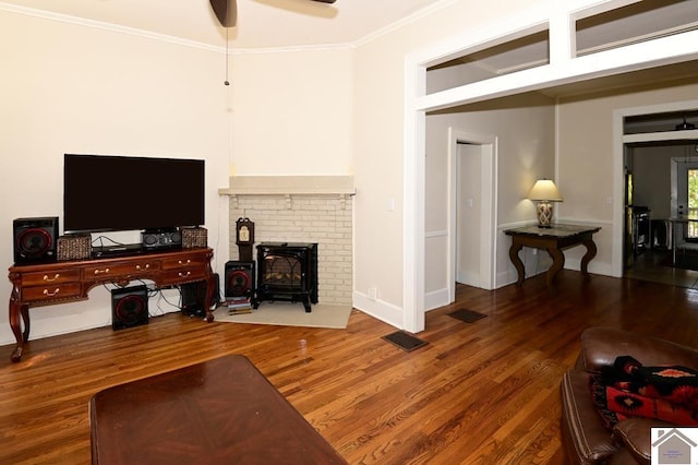 living room featuring a wood stove, ceiling fan, wood-type flooring, and crown molding