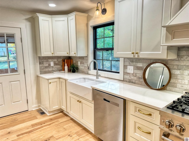 kitchen with white cabinetry, sink, light hardwood / wood-style flooring, decorative backsplash, and appliances with stainless steel finishes