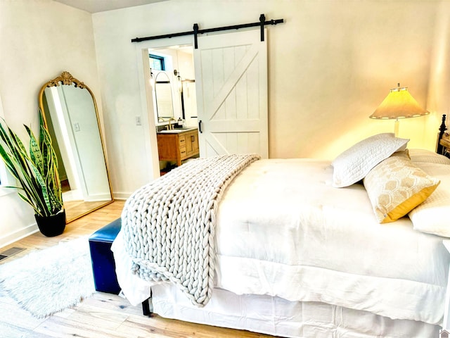 bedroom featuring a barn door, light wood-type flooring, and connected bathroom