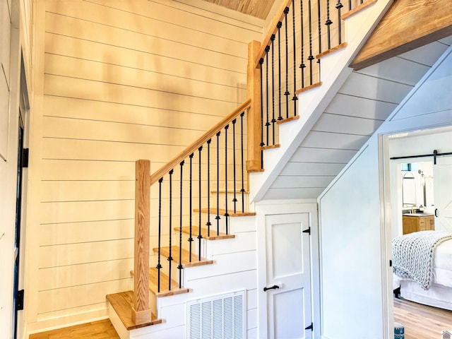 stairs featuring hardwood / wood-style floors, wood walls, a barn door, and wood ceiling