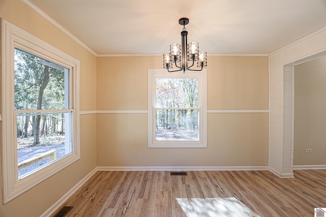 unfurnished dining area featuring crown molding, hardwood / wood-style flooring, an inviting chandelier, and plenty of natural light