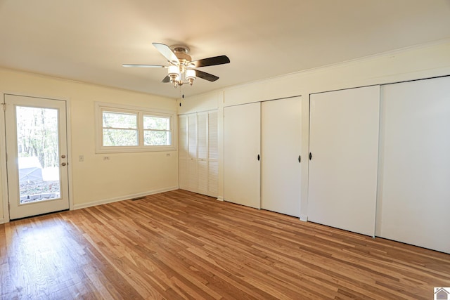 unfurnished bedroom featuring crown molding, two closets, light wood-type flooring, and ceiling fan