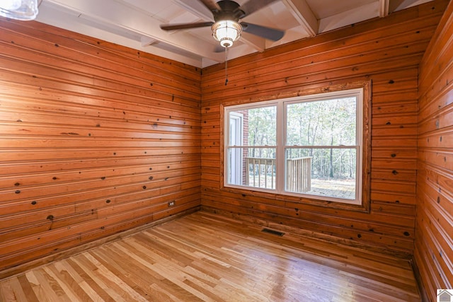 empty room with beam ceiling, wood walls, and light hardwood / wood-style flooring