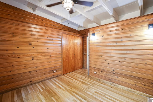 spare room featuring vaulted ceiling with beams, wood walls, light wood-type flooring, and ceiling fan