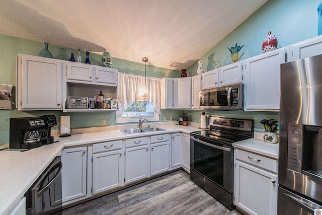 kitchen with lofted ceiling, hanging light fixtures, stainless steel appliances, sink, and white cabinetry