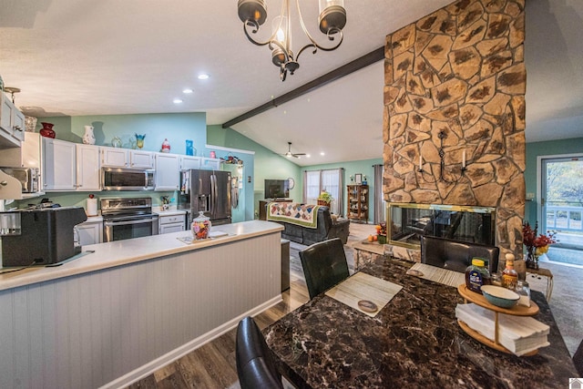 kitchen with a stone fireplace, stainless steel appliances, hardwood / wood-style floors, lofted ceiling with beams, and white cabinets