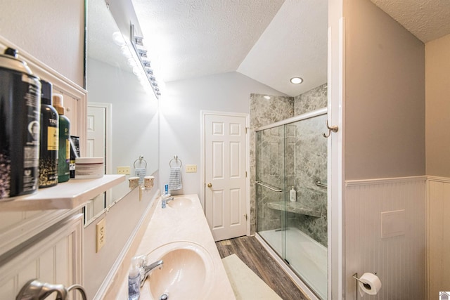 bathroom with a shower with door, lofted ceiling, hardwood / wood-style flooring, vanity, and a textured ceiling