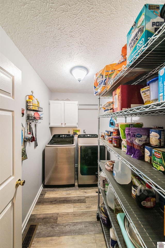 laundry area with washer and dryer, a textured ceiling, light hardwood / wood-style floors, and cabinets