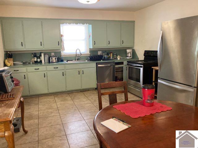 kitchen featuring appliances with stainless steel finishes, sink, light tile patterned floors, and green cabinetry