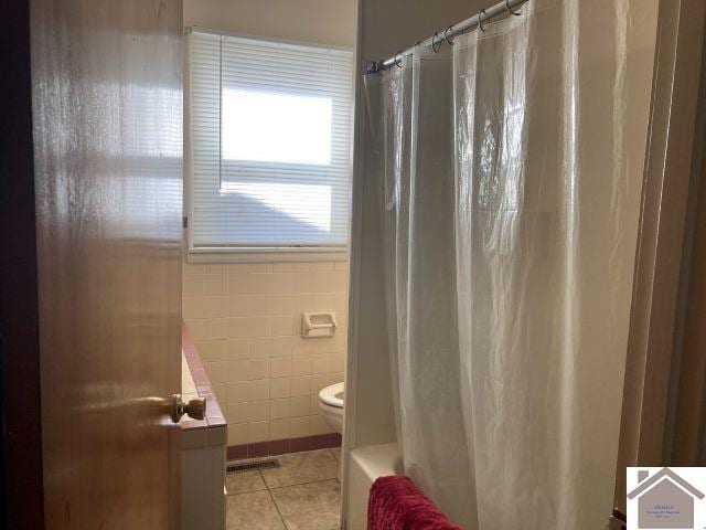 bathroom featuring toilet, shower / bath combo with shower curtain, tile walls, and tile patterned flooring