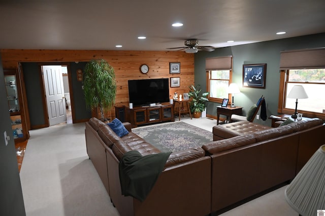 living room with light carpet, wood walls, ceiling fan, and a wealth of natural light