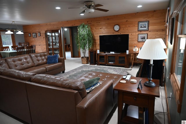 carpeted living room with ceiling fan and wood walls