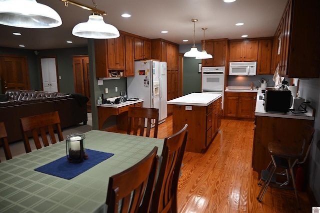 kitchen with a center island, decorative light fixtures, light wood-type flooring, and white appliances