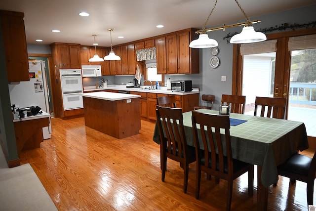 kitchen featuring a kitchen island, light hardwood / wood-style floors, hanging light fixtures, sink, and white appliances