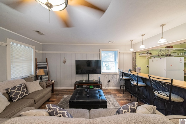 living room with ornamental molding, wooden walls, dark hardwood / wood-style floors, and ceiling fan