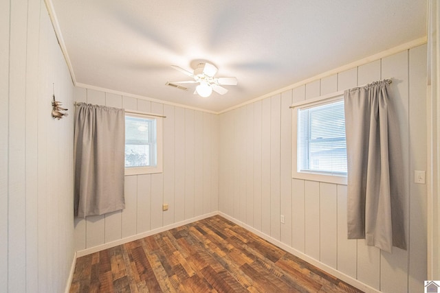 spare room with dark wood-type flooring, wood walls, ceiling fan, and crown molding