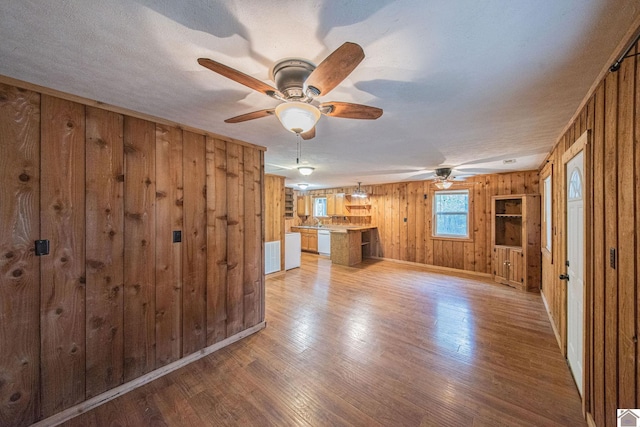 unfurnished living room with light hardwood / wood-style floors, wood walls, a textured ceiling, and ceiling fan