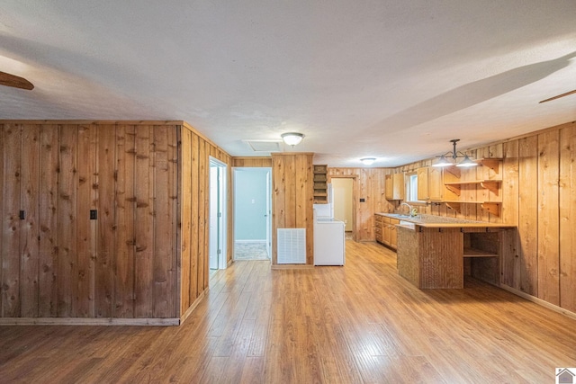 kitchen with wood walls, kitchen peninsula, sink, and light hardwood / wood-style floors