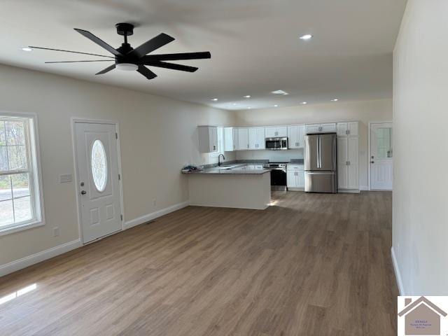 kitchen with dark wood-type flooring, kitchen peninsula, ceiling fan, white cabinetry, and appliances with stainless steel finishes