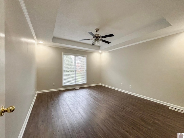 empty room with ceiling fan, a tray ceiling, dark hardwood / wood-style floors, and crown molding