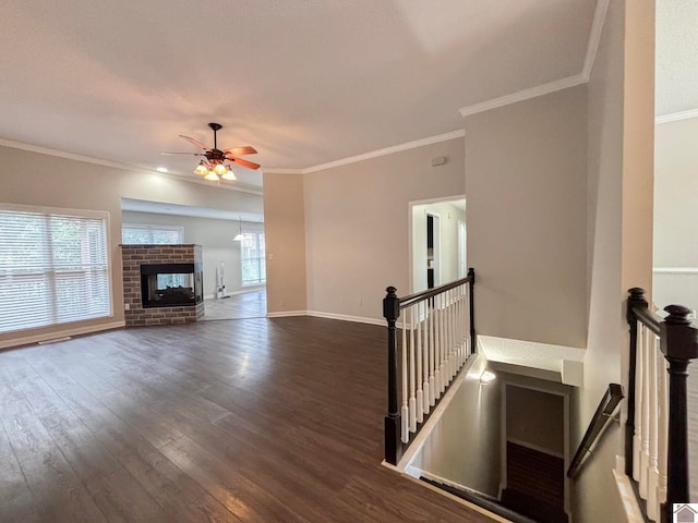 unfurnished living room with dark wood-type flooring, ceiling fan, crown molding, and a brick fireplace