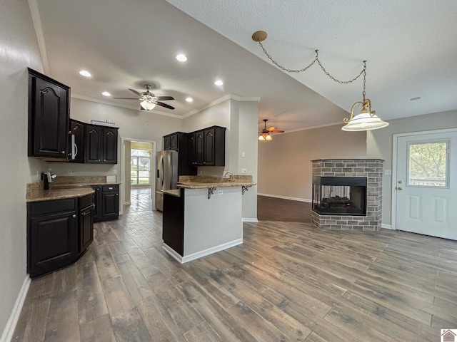 kitchen with a breakfast bar, kitchen peninsula, ceiling fan, stainless steel fridge with ice dispenser, and dark hardwood / wood-style flooring