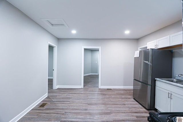 kitchen featuring white cabinetry, light wood-type flooring, stainless steel refrigerator, sink, and black range oven