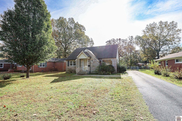 view of front facade featuring aphalt driveway, a front lawn, fence, and brick siding