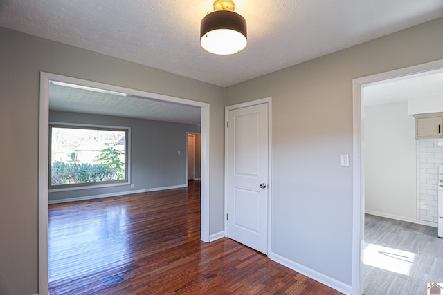 unfurnished room with a textured ceiling, baseboards, and wood finished floors