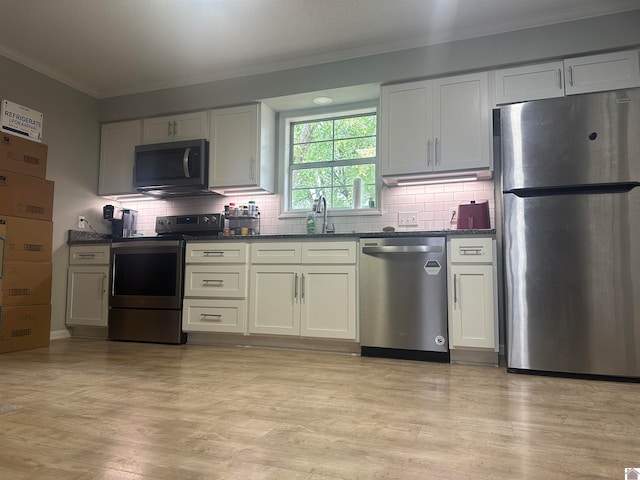 kitchen with ornamental molding, light wood-type flooring, appliances with stainless steel finishes, decorative backsplash, and white cabinets