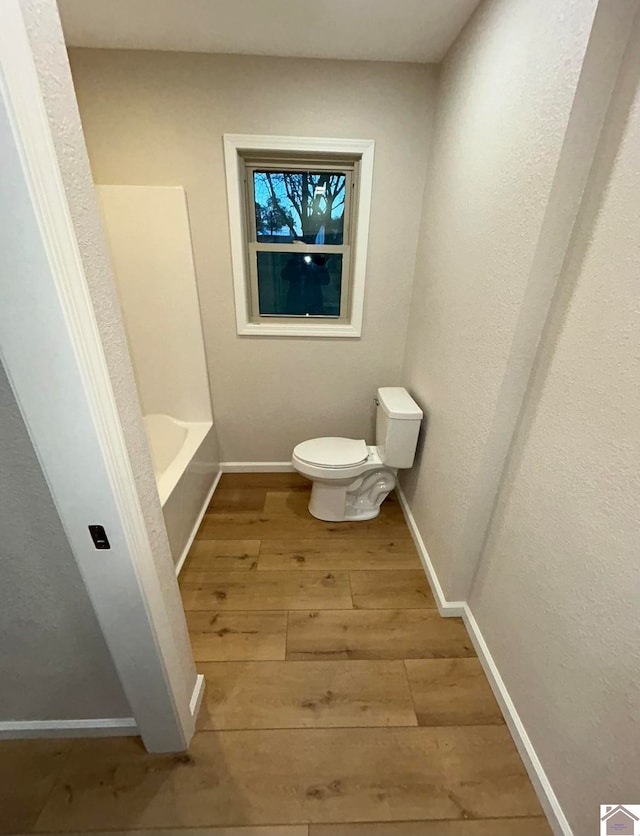 bathroom with toilet, a washtub, and wood-type flooring