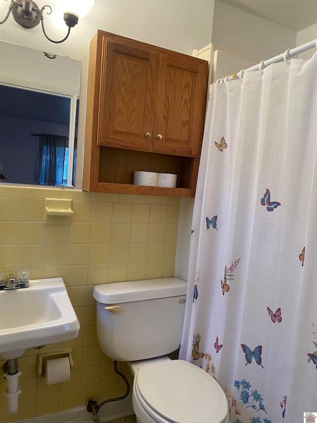 bathroom with tile walls, curtained shower, sink, and toilet