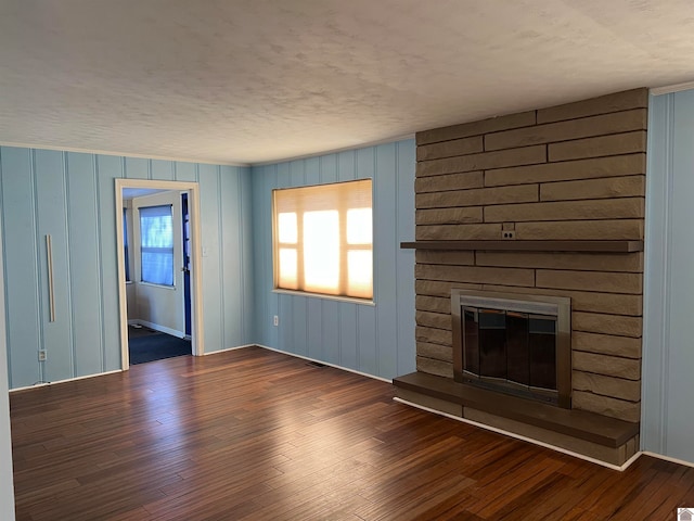 unfurnished living room with a large fireplace, dark wood-type flooring, and wood walls