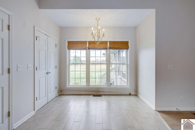 unfurnished dining area featuring a textured ceiling, light hardwood / wood-style floors, and a chandelier