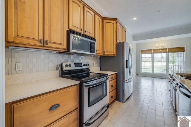 kitchen with a chandelier, tasteful backsplash, sink, ornamental molding, and appliances with stainless steel finishes