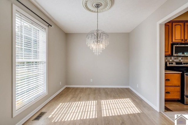 unfurnished dining area featuring an inviting chandelier and light hardwood / wood-style flooring