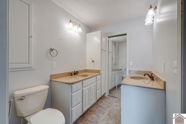 bathroom with tile patterned flooring, vanity, a textured ceiling, and toilet