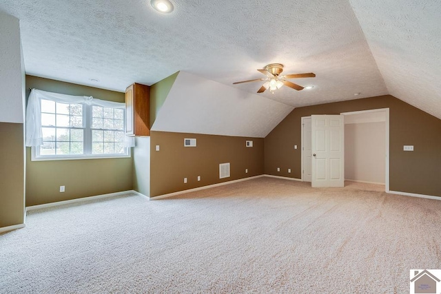 bonus room with a textured ceiling, light colored carpet, lofted ceiling, and ceiling fan