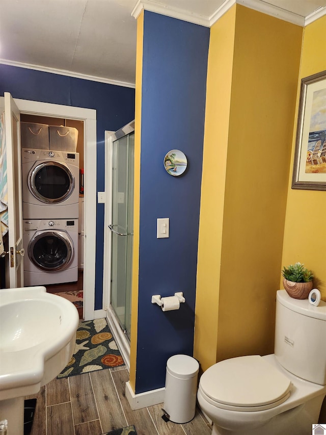 bathroom with a shower with door, crown molding, stacked washer and dryer, hardwood / wood-style flooring, and toilet