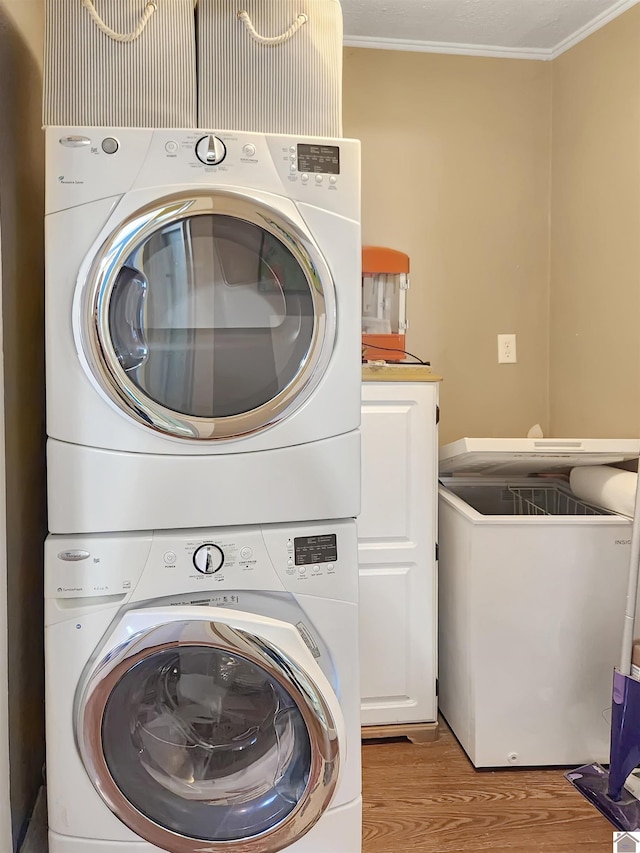 washroom featuring cabinets, light hardwood / wood-style floors, stacked washer and clothes dryer, and crown molding