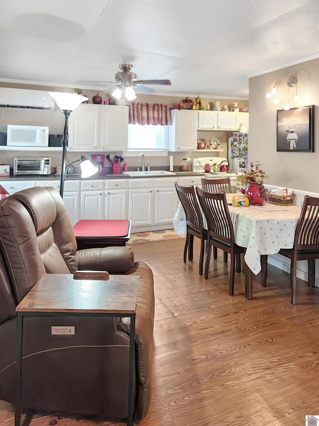 kitchen with a wall mounted AC, light wood-type flooring, sink, white cabinets, and white appliances