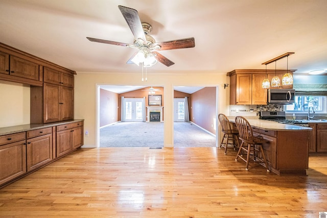 kitchen with a breakfast bar area, ceiling fan, light wood-type flooring, appliances with stainless steel finishes, and decorative light fixtures