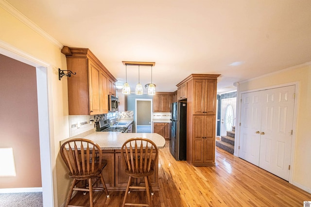 kitchen featuring crown molding, light wood-type flooring, appliances with stainless steel finishes, decorative backsplash, and kitchen peninsula