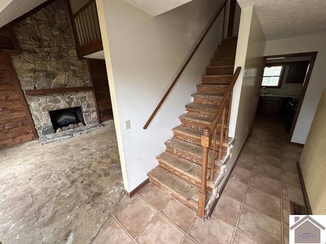 stairs with a stone fireplace and a textured ceiling