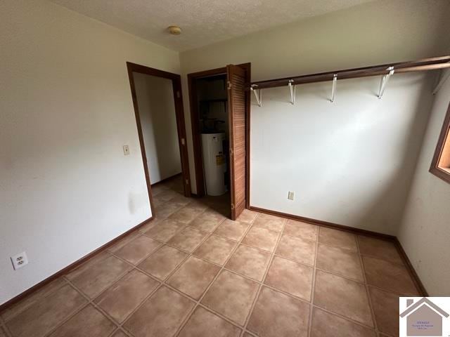 unfurnished bedroom featuring water heater, a textured ceiling, and light tile patterned floors