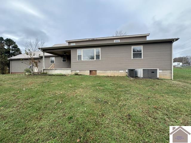 rear view of house featuring central AC unit and a yard